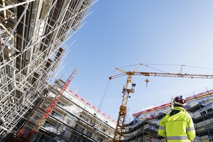 Chantier de construction extérieur avec ouvrier en veste haute visibilité jaune observant les travaux