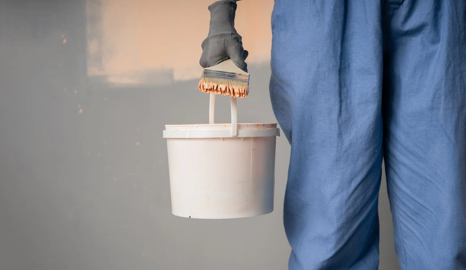 Peintre professionnel en salopette et casquette blanches appliquant de la peinture jaune sur un mur intérieur avec un rouleau à peinture
