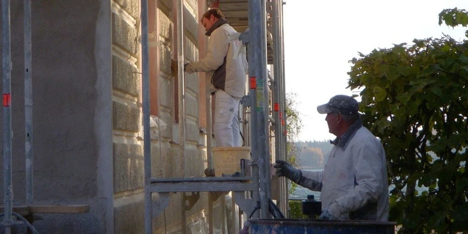 Deux professionnels du bâtiment en vêtements de sécurité se serrent la main dans un bureau lumineux près d'une fenêtre, symbolisant un accord ou partenariat