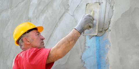 Ouvrier du bâtiment appliquant du plâtre sur les murs avec une truelle, présentant un savoir-faire artisanal dans la rénovation de la maison