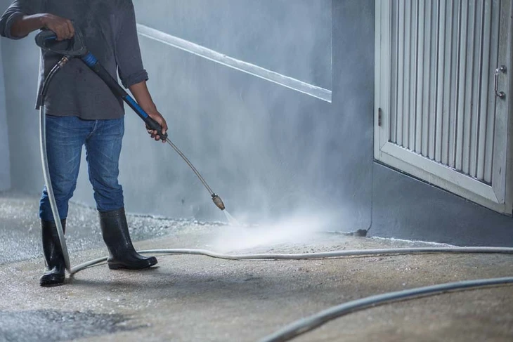 Homme en vêtements de travail utilisant un nettoyeur haute pression sur une surface bétonnée extérieure