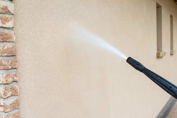 Nettoyage haute pression d'un mur extérieur en crépi beige avec jet d'eau puissant