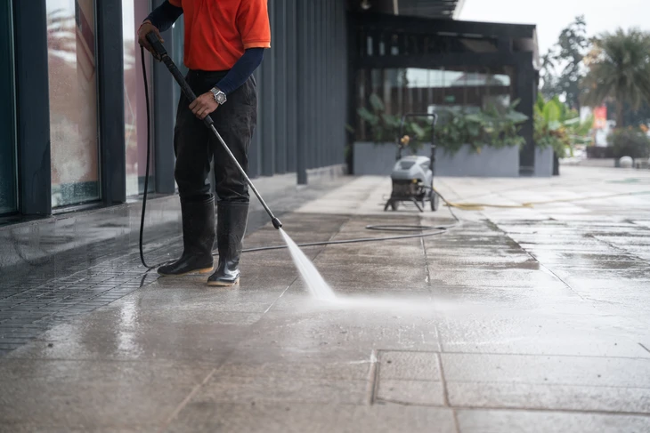 le personnel de nettoyage rince une voiture portative pour laver le sol en béton avec des jets d'eau haute pression