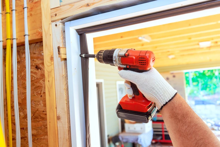 Chantier de construction intérieur avec ouvrier utilisant une perceuse-visseuse sans fil rouge pour fixer une fenêtre PVC blanc
