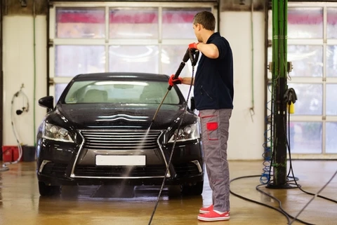 Un homme lave une berline noire Lexus dans un garage automobile professionnel