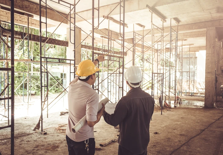 Chantier de construction intérieur avec deux professionnels en casques de sécurité jaune et blanc consultant des plans architecturaux