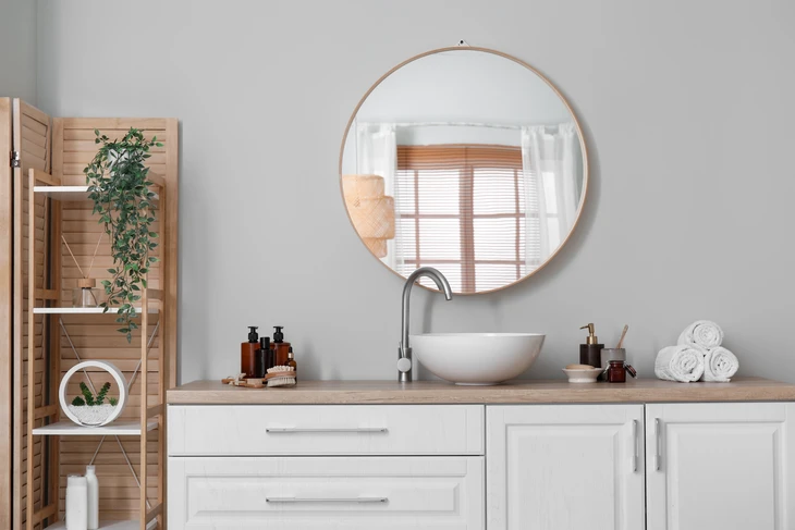 Salle de bain moderne avec vasque à poser blanche sur plan de travail bois, robinetterie chromée contemporaine, miroir rond avec cadre doré