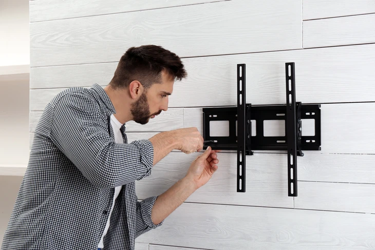Homme installant un support mural TV noir sur mur en bois blanc