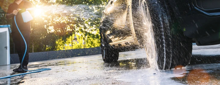 Scène extérieure de lavage automobile avec jet d'eau haute pression pulvérisé sur véhicule