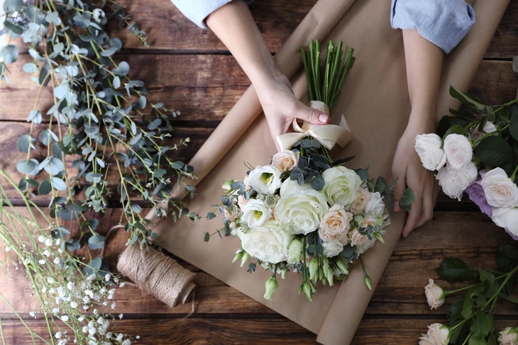 Scène d'atelier floral intérieur avec mains féminines assemblant un bouquet sur plan de travail en bois