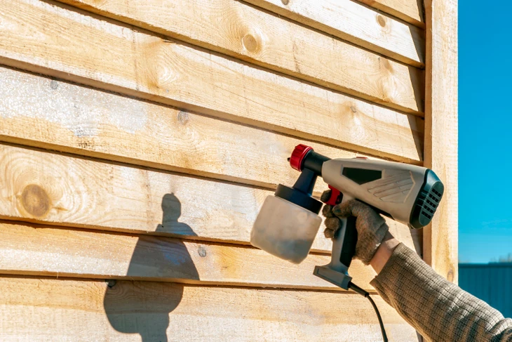 Extérieur ensoleillé, personne appliquant un traitement sur bardage bois horizontal
