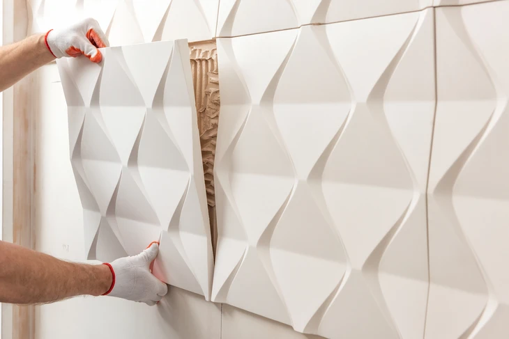 Ouvrier installant des panneaux muraux décoratifs 3D blancs à motifs géométriques sur mur intérieur
