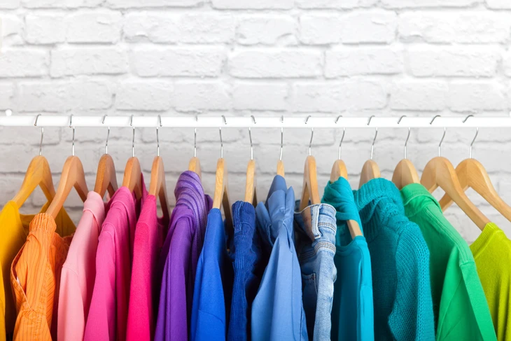 Intérieur avec mur de briques blanches, portant en métal blanc supportant une collection de vêtements colorés suspendus sur cintres en bois naturel