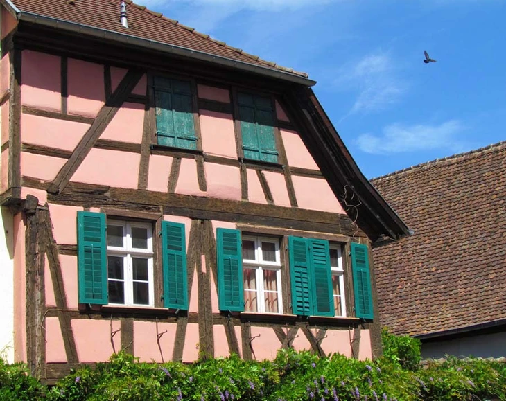 Façade extérieure d'une maison alsacienne traditionnelle à colombages avec murs roses et poutres apparentes en bois foncé