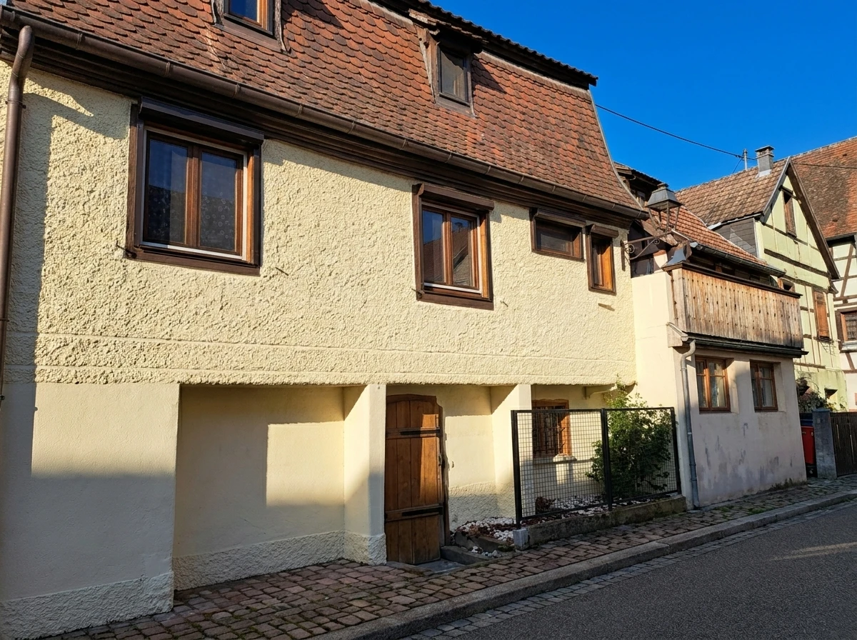 Façade extérieure d'une maison alsacienne traditionnelle à colombages avec murs roses et poutres apparentes en bois foncé