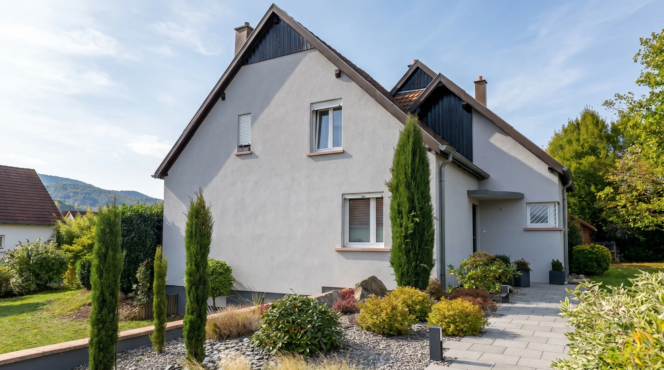 Maison contemporaine avec façade en crépi beige et toit en tuiles grises, dotée de fenêtres de toit velux