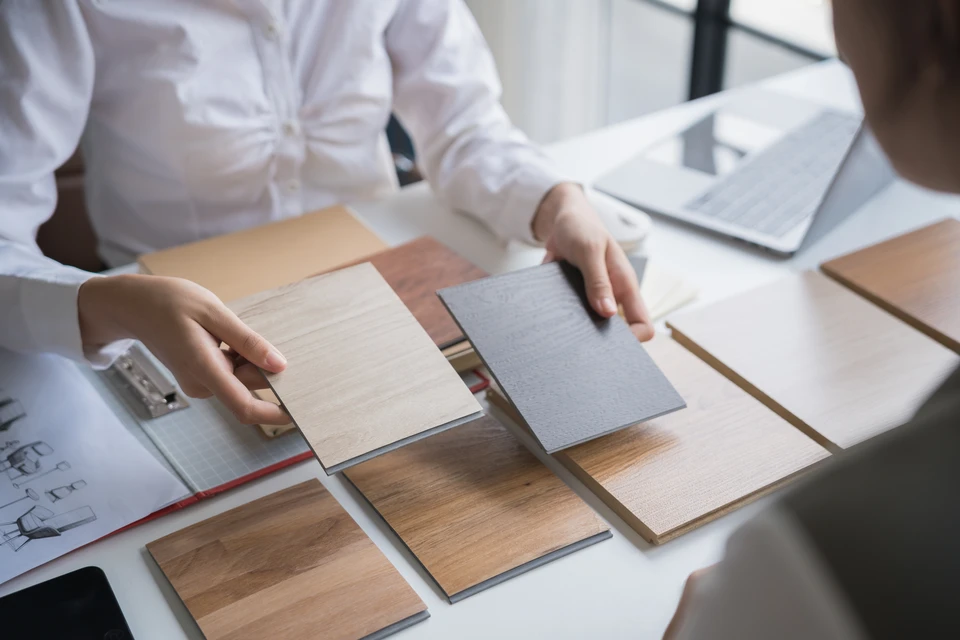 Photographie réaliste d'un artisan en tenue de travail (polo ou chemise professionnelle) discutant avec un client à l'intérieur d'un logement, pointant ou examinant un mur, une façade intérieure, ou des zones nécessitant rénovation. L'artisan consulte ses notes ou un document devis. La scène se déroule dans un cadre résidentiel authentique, montrant l'analyse technique et le conseil personnalisé du professionnel auprès du client.
